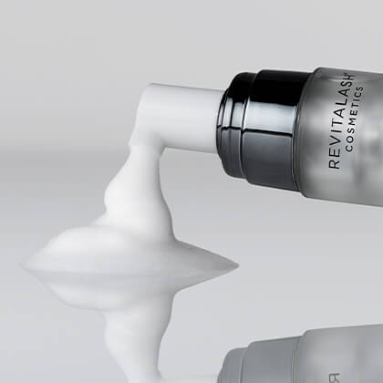 Revitalash cosmetic bottle with white cream being squeezed out on a light gray background